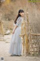 A woman in a blue dress standing next to a wooden fence.