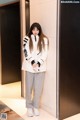 A woman standing in an elevator wearing a white jacket and grey sweatpants.