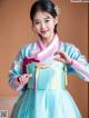 A woman in a blue and pink hanbok poses for a picture.