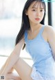 A woman in a blue tank top sitting on a window sill.