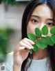 A woman holding a green leaf in front of her face.