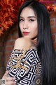 A woman with long black hair standing in front of a brick wall.