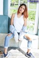 A woman sitting on a window sill wearing ripped jeans and a white tank top.