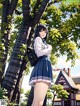 A girl in a school uniform standing next to a tree.