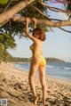 A woman in a yellow bikini standing on a beach.