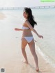 A woman in a white bikini walking on the beach.