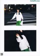 A woman in a white sweatshirt and green skirt standing on a crosswalk.