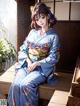 A woman in a blue kimono sitting on a wooden bench.