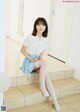 A woman in a white shirt and blue skirt sitting on the stairs.