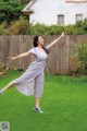 A woman in a gray dress is dancing in the grass.